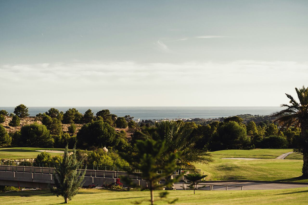 Golf course fairways among pines and palm trees, with the Mediterranean beyond