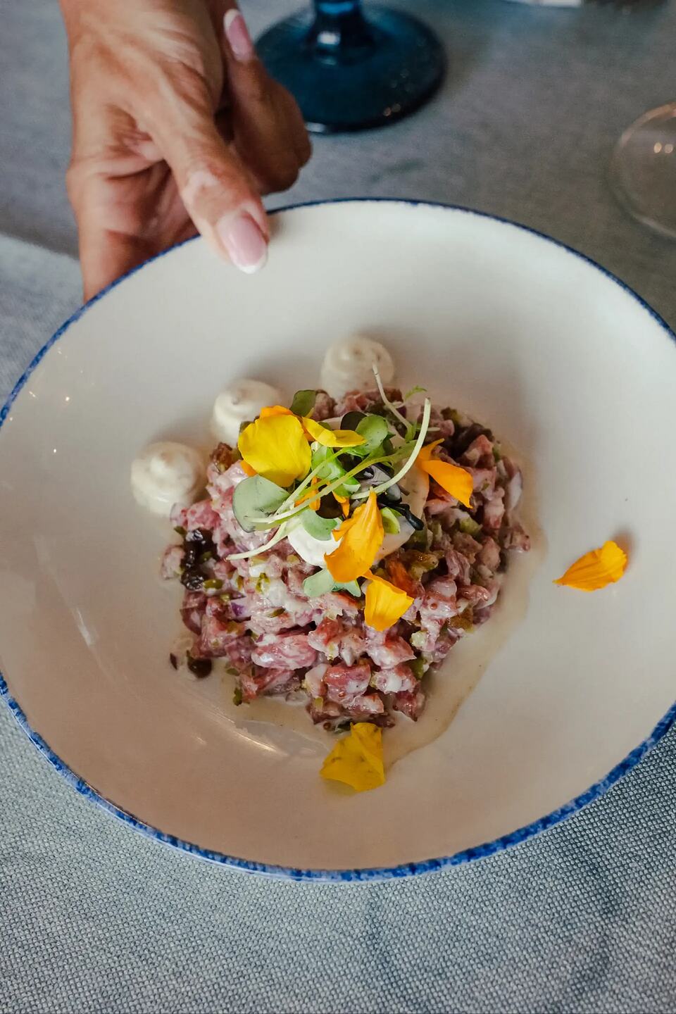 Beef tartare garnished with yellow edible flowers and microgreens in a white bowl