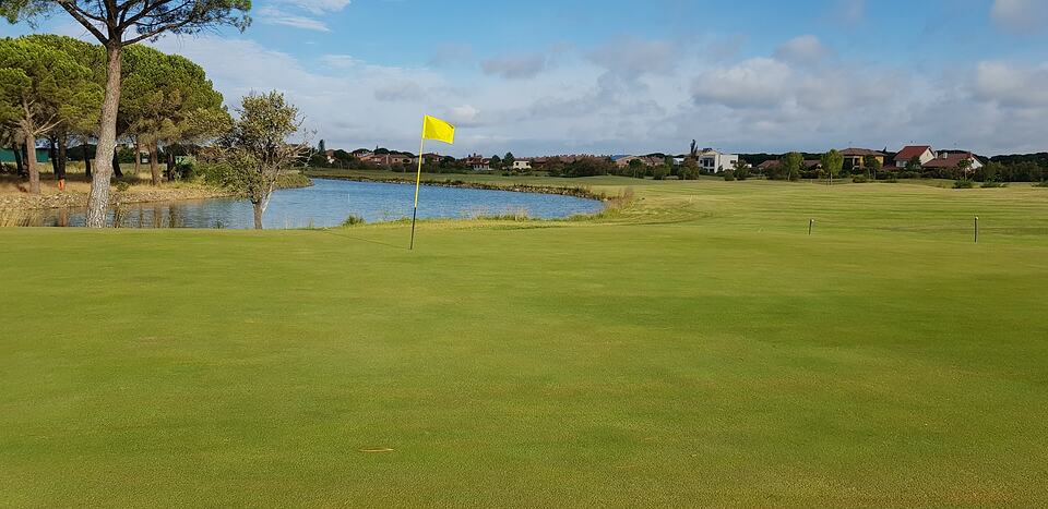 A golf green with a yellow flag beside a pond at Aldeamayor Club de Golf