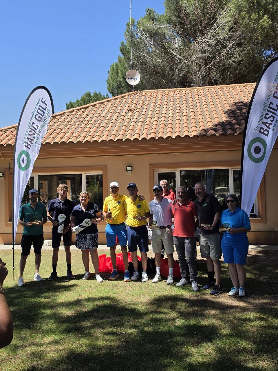 A group of golfers poses outside the clubhouse between banners for the Basic Golf event.