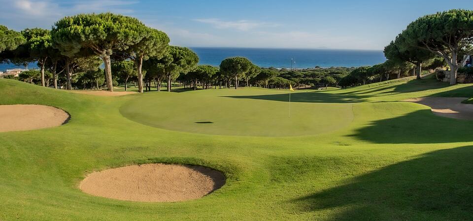 A Cabopino Golf green with sand bunkers, pine trees and the sea in the background