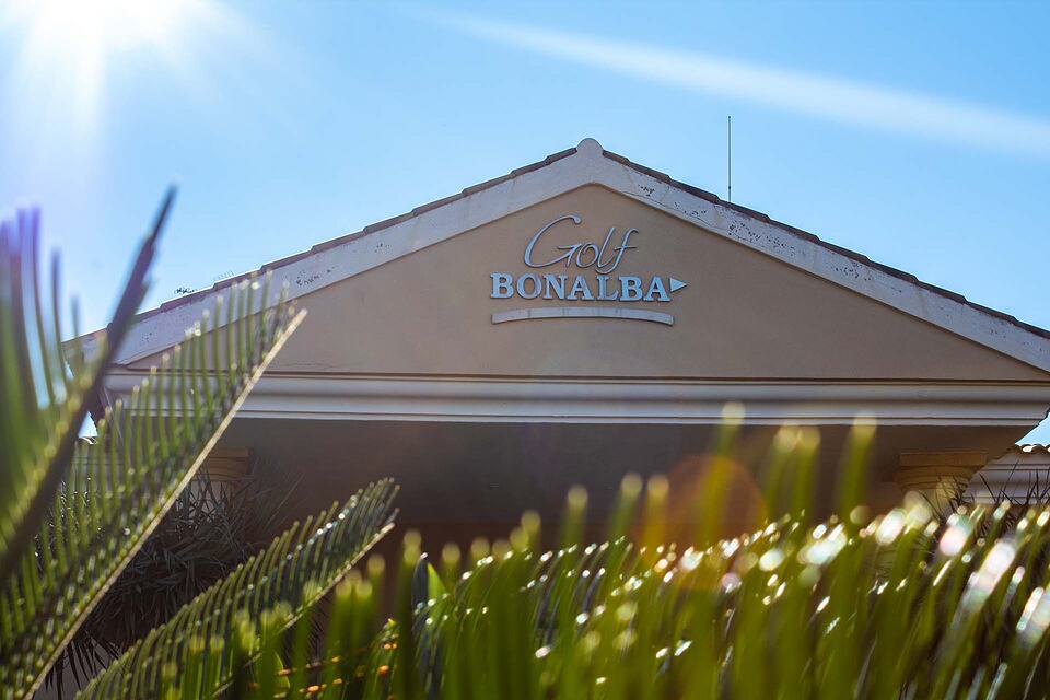 Nombre de Golf Bonalba en la fachada de la casa club, enmarcada por hojas de palmera