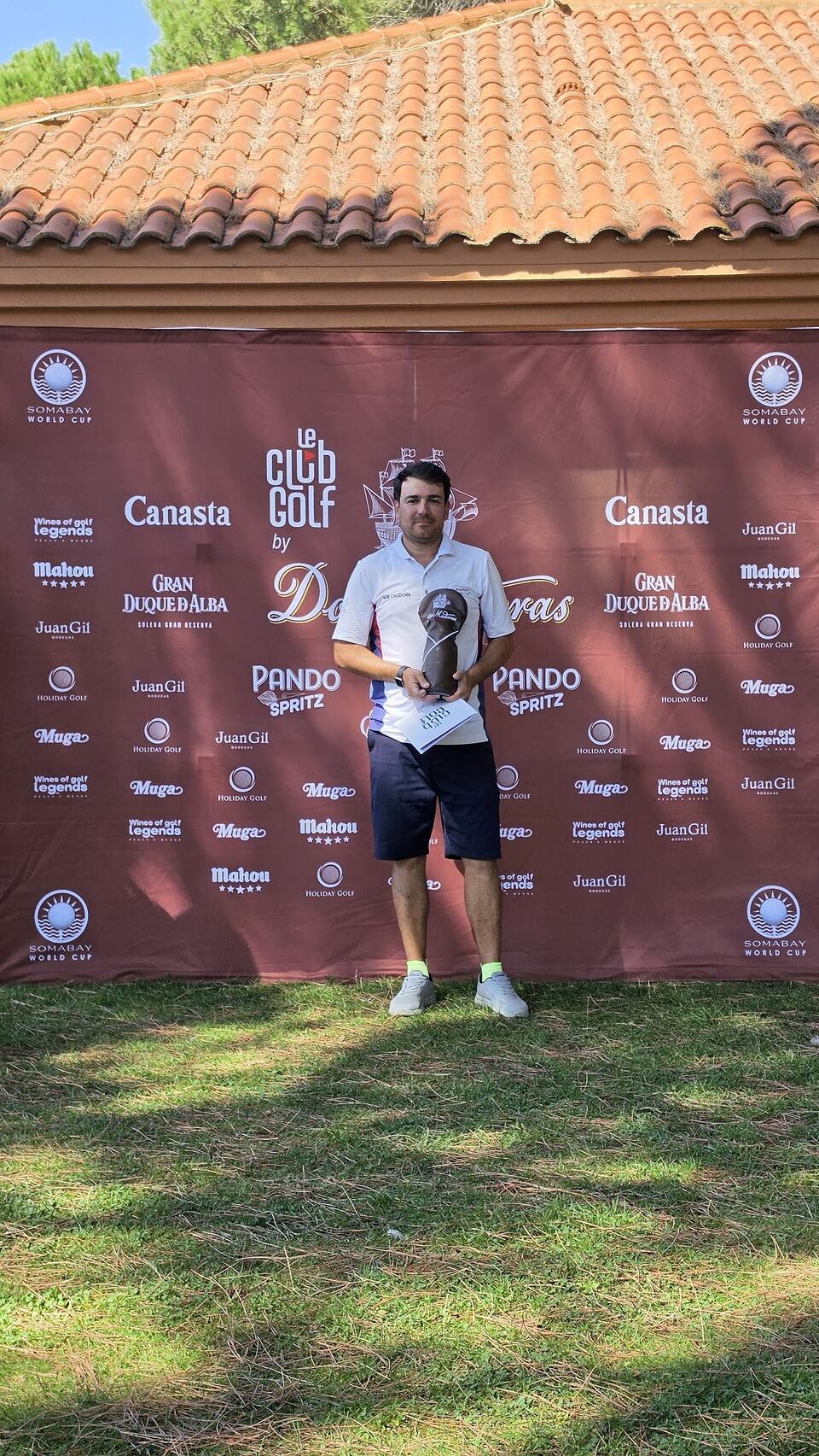 Ganador de un torneo de golf con trofeo y diploma ante un fondo de patrocinadores