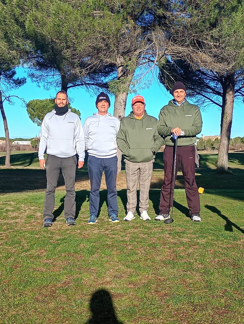 Four golfers pose on the course beneath pine trees.