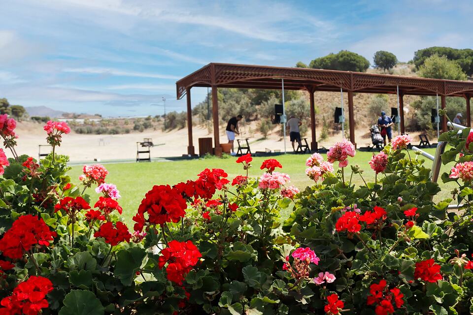 Baviera Golf practice range with golfers under a wooden shelter and flowers in the foreground