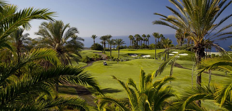 Campo de golf entre palmeras, con bunkers y el mar al fondo