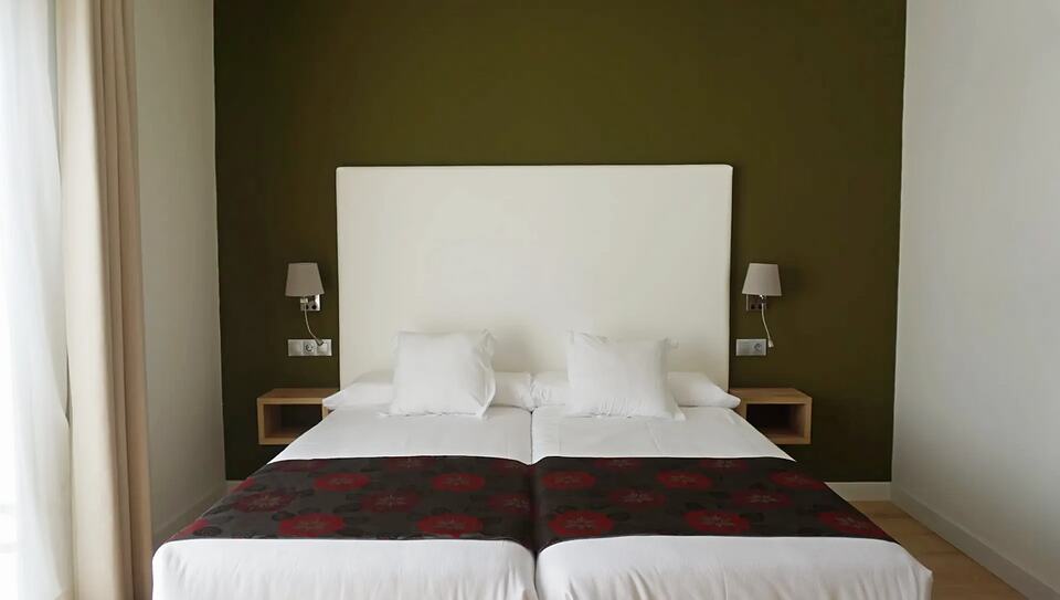 Hotel room with a double bed, white headboard and olive-green accent wall