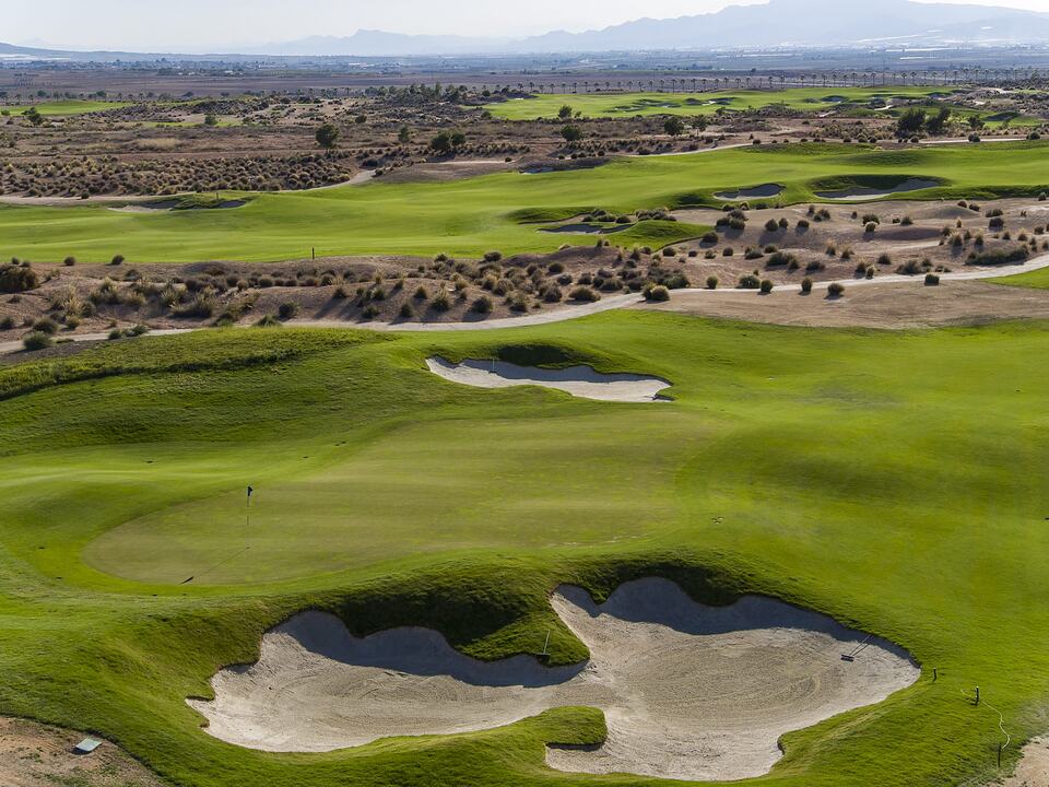 Campo de Alhama Signature Golf con calles onduladas y búnkeres, con montañas al fondo