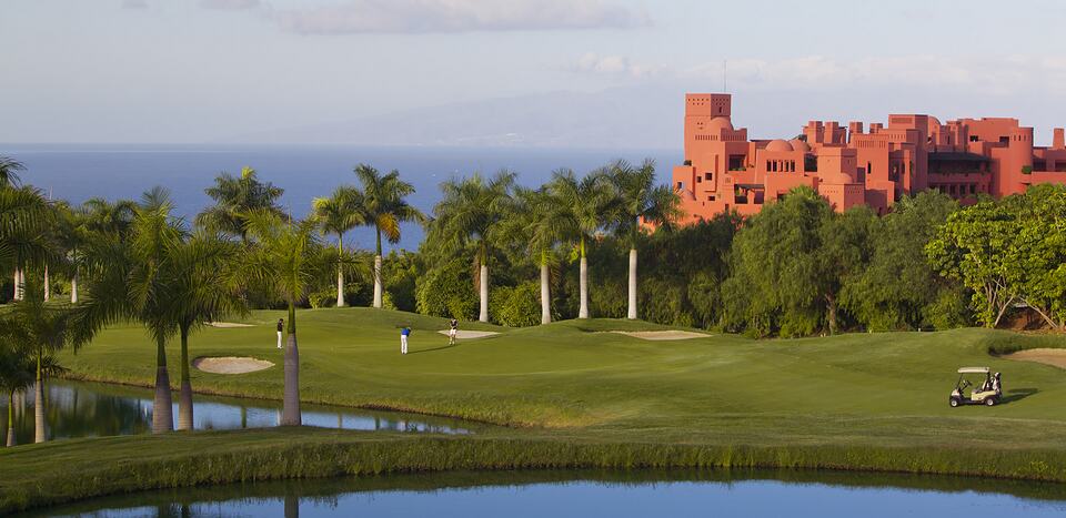 Campo de golf de Abama con palmeras, un lago y los edificios del resort junto al mar