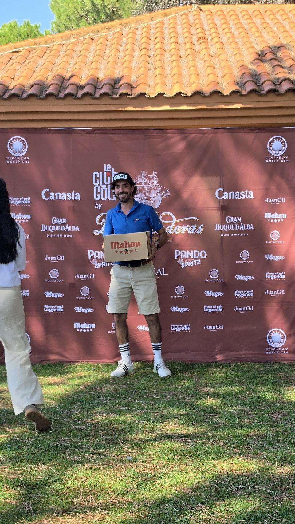 Ganador de un torneo de golf con un premio Mahou ante un fondo de patrocinadores