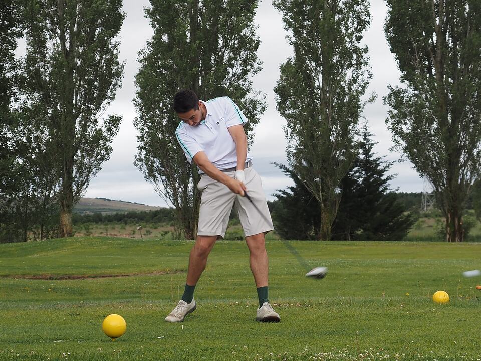 A golfer practices a drive on the grass beside yellow tee markers.