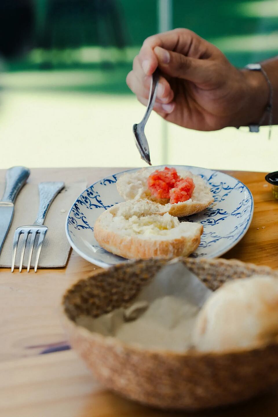Bread with grated tomato on a plate as a hand prepares breakfast at a restaurant table