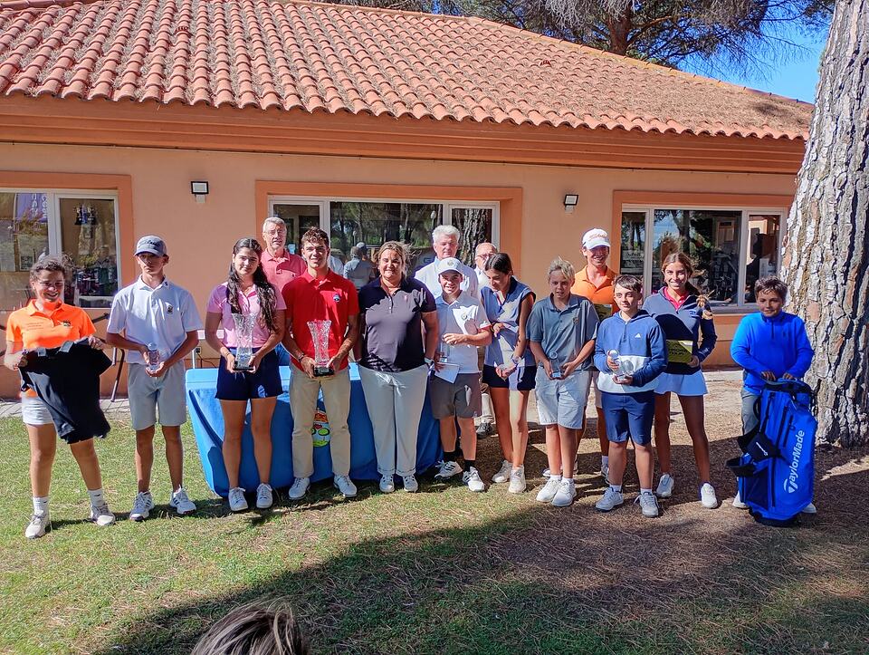 A group of young golfers and adults pose with trophies outside the clubhouse.