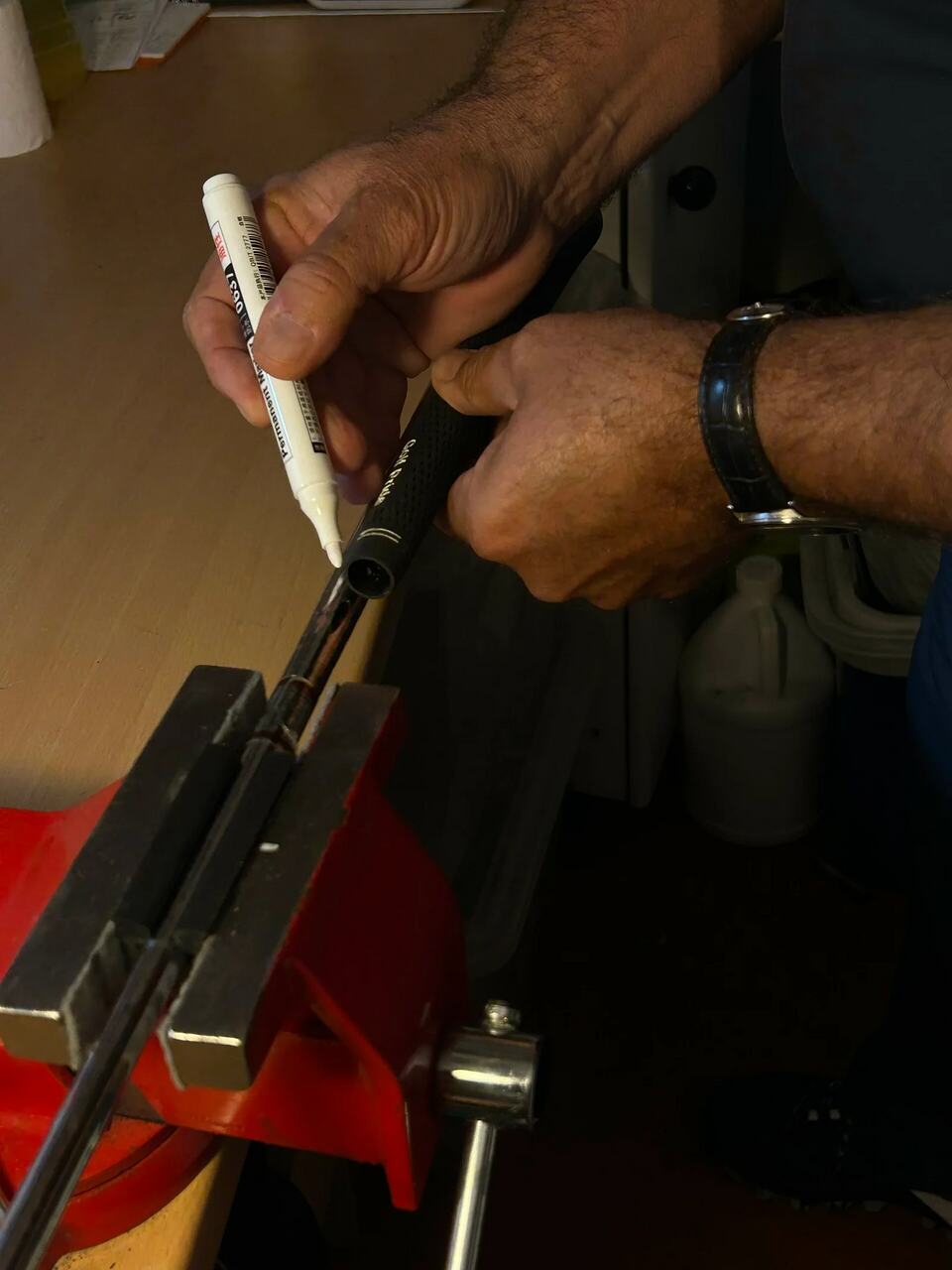 Hands marking a golf club shaft held in a workshop vise