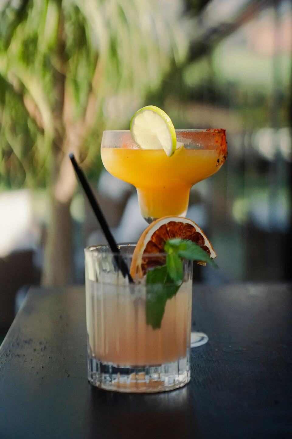 Two cocktails garnished with lime, dried orange, and mint on a table