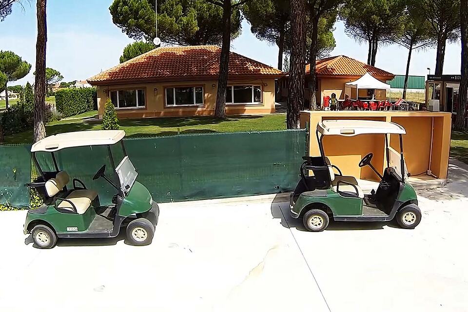 Two golf carts parked outside the clubhouse at Aldeamayor Golf Club.