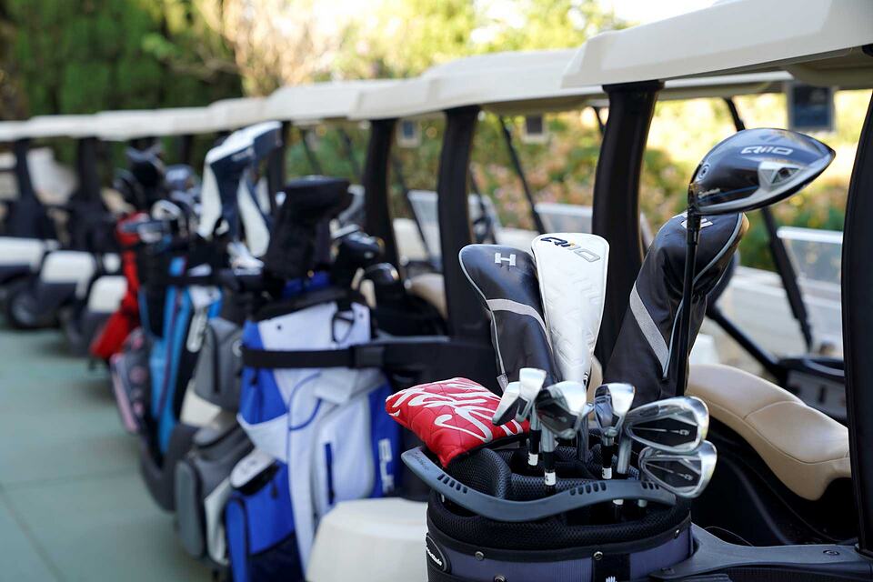 Golf clubs and bags lined up in a row of golf carts.