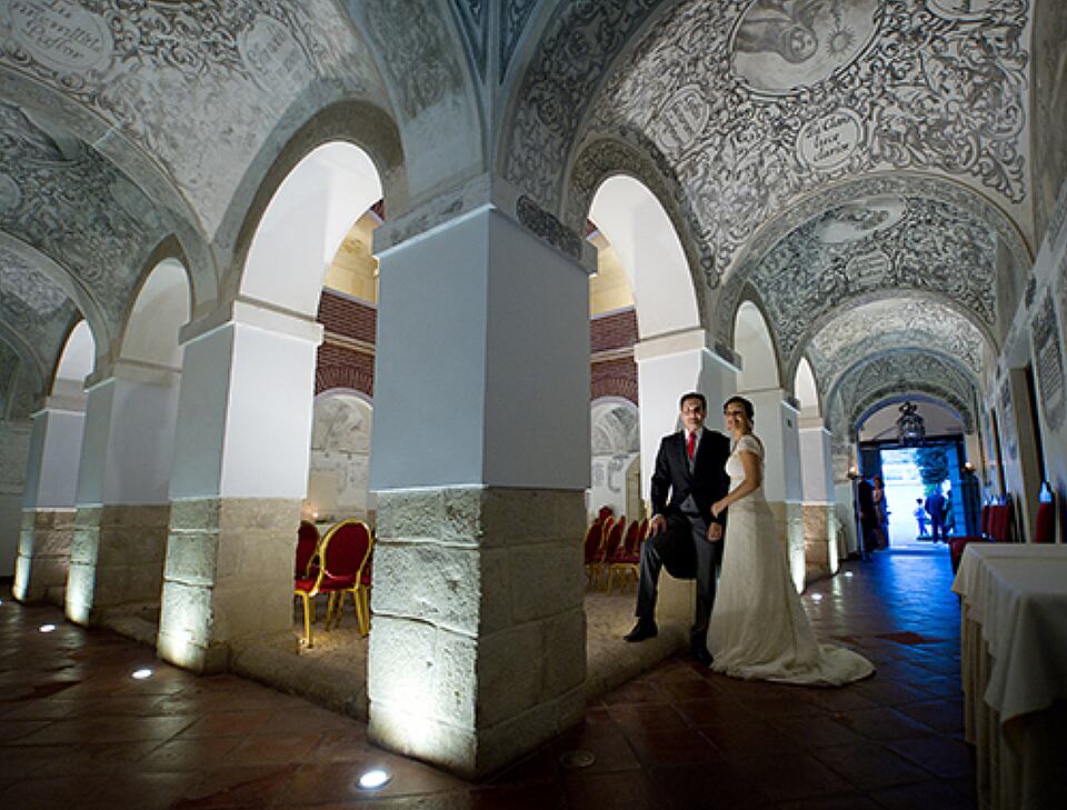 Bride and groom in an ornate vaulted hall set up for a social event.