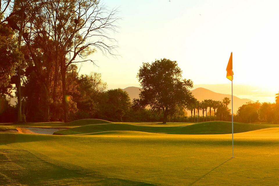 Golf green with a yellow flag at sunset, trees and hills in the background