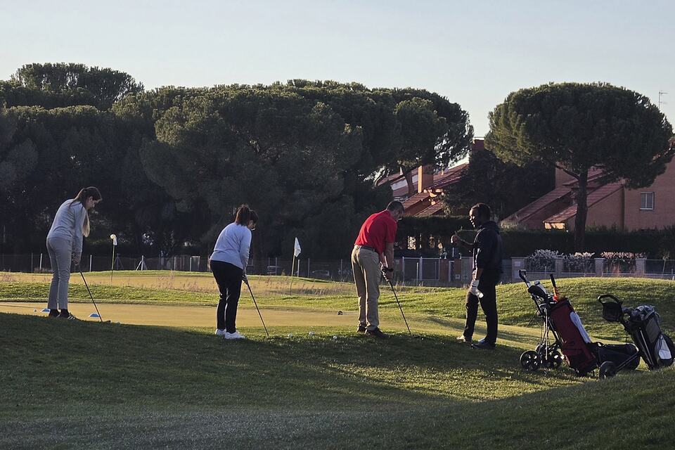 Golfers practicing putting on a green while an instructor gives guidance.