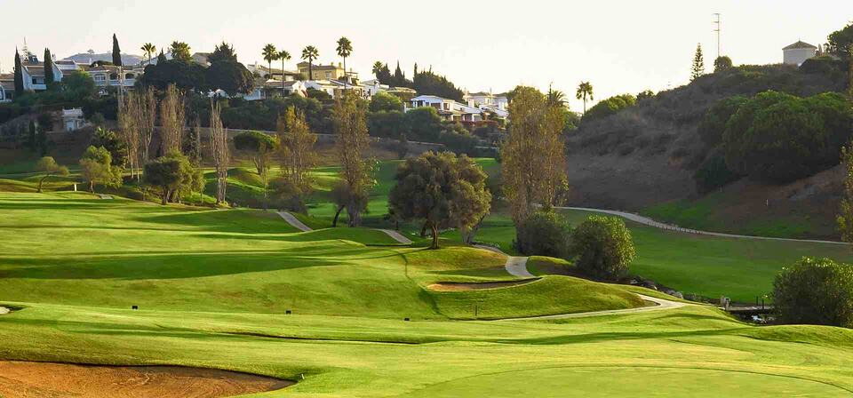 Rolling fairways and greens at Cabopino Golf Marbella, with hillside homes and trees in the background