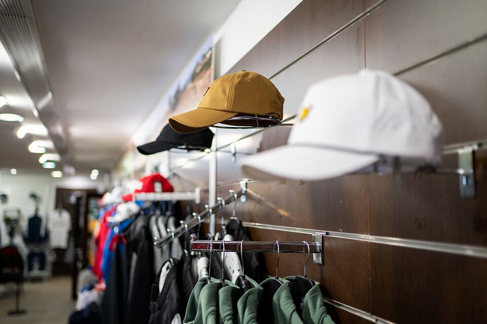 Golf caps and clothing displayed on shelves and racks inside the pro shop.