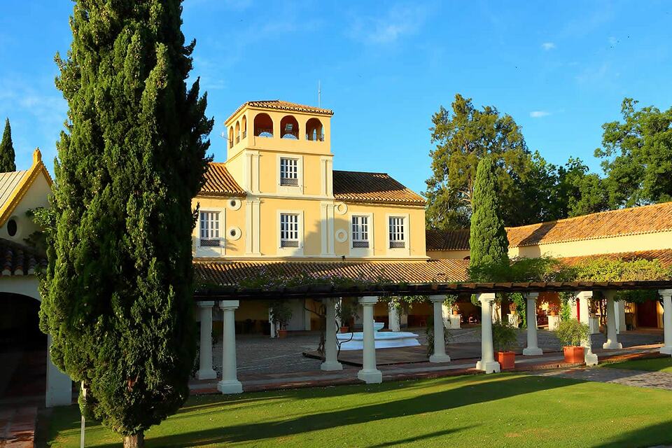 Yellow Andalusian-style clubhouse with a tiled roof, columned courtyard and cypress trees