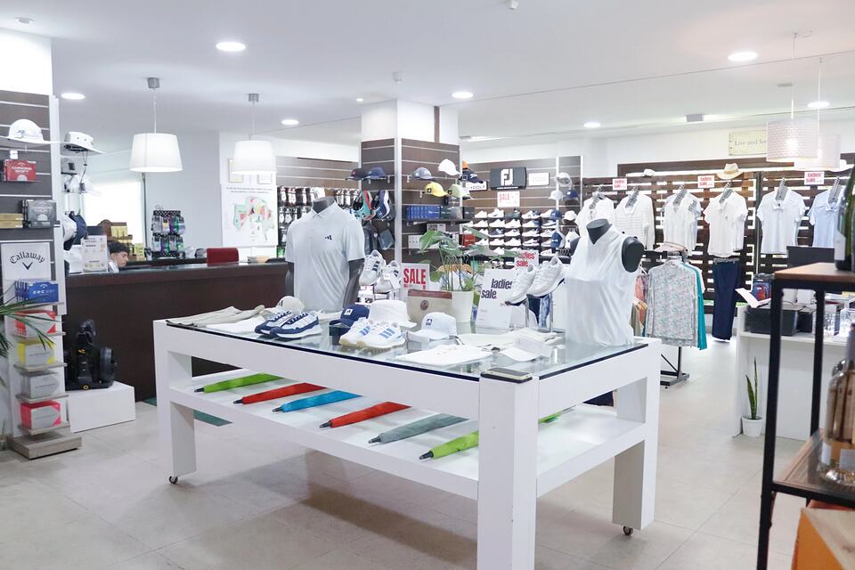 Bright golf shop with clothing, shoes, hats and accessories displayed on shelves and tables.