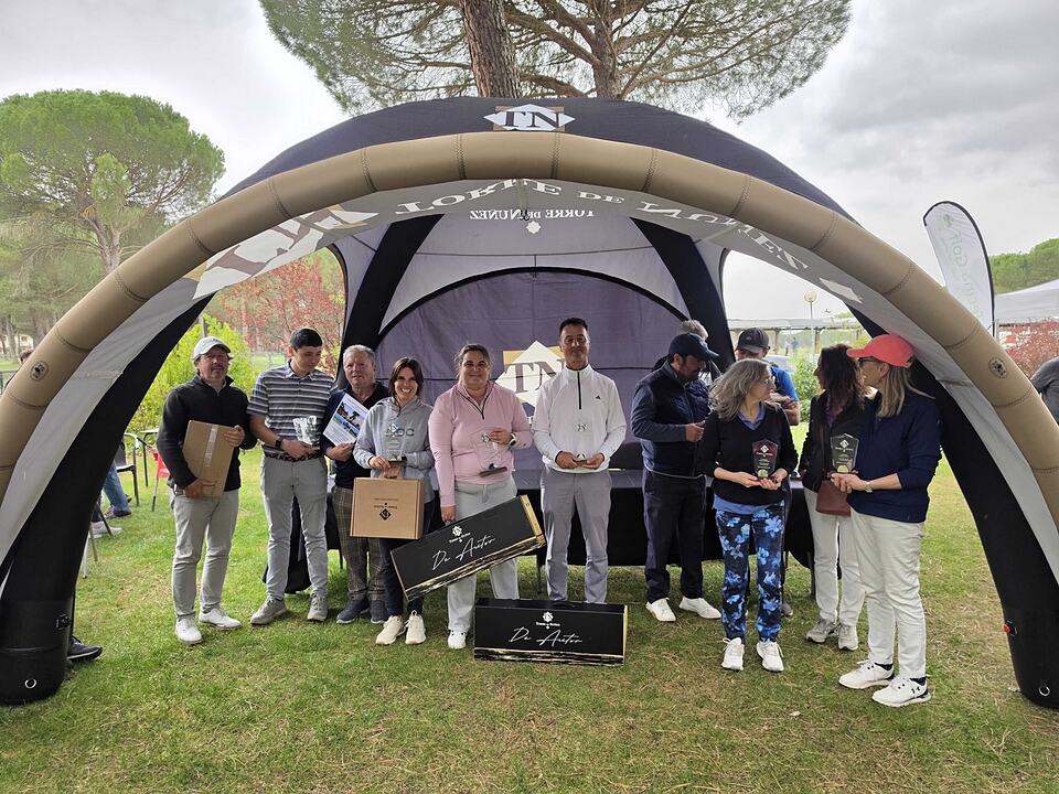 Golf event participants pose with prizes beneath an inflatable tent at Aldeamayor Club de Golf.
