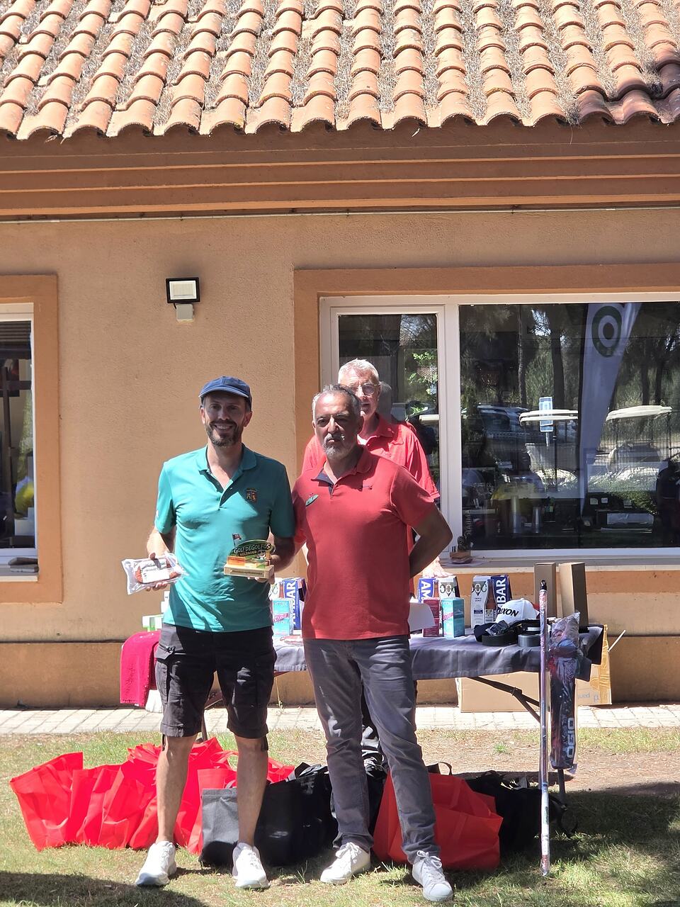 Golf tournament participants pose with prizes beside a display table outside the clubhouse.