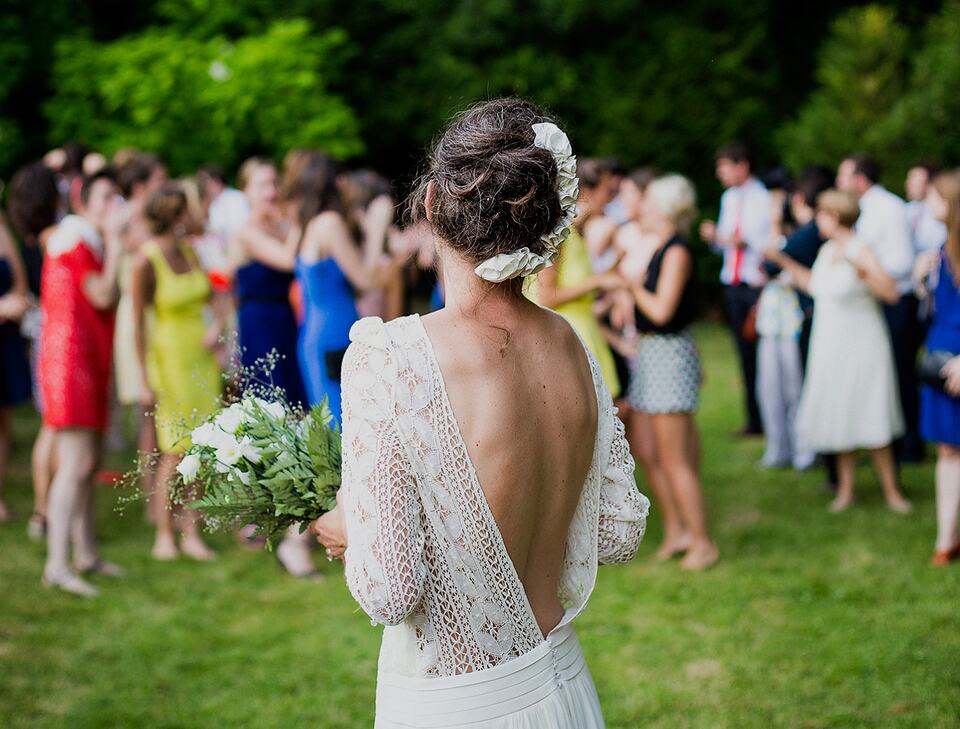 Bride holding a bouquet at an outdoor wedding reception with guests gathered on the lawn