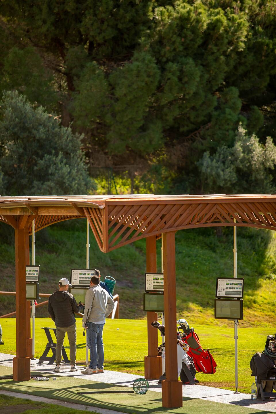 Golfers at covered practice bays on Baviera Golf’s driving range.