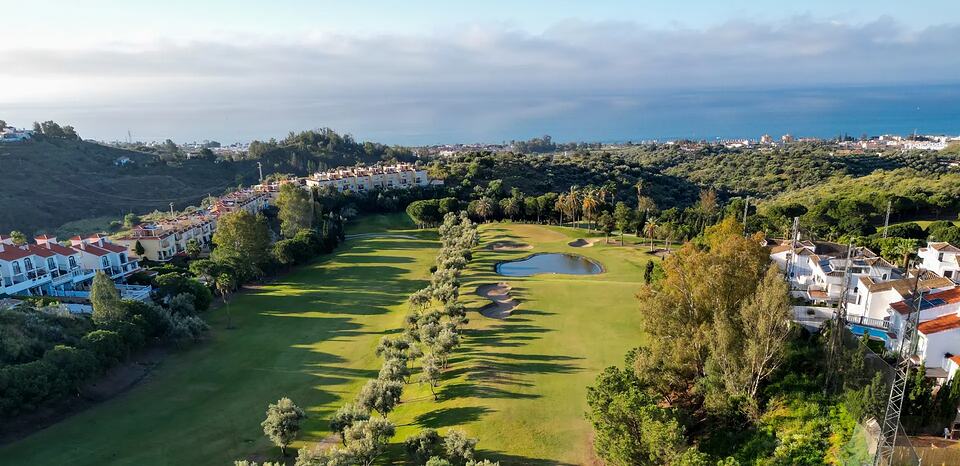 Aerial view of a golf course with a pond and the sea on the horizon