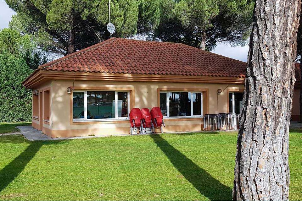 Low clubhouse building with a red-tiled roof among pine trees