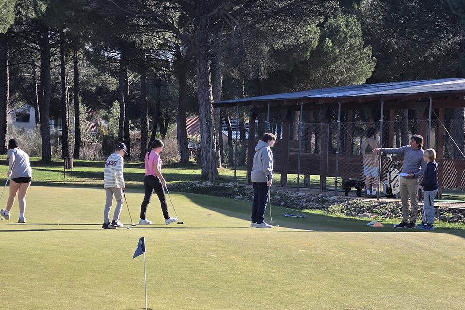 Golf students practice putting on a green while an instructor gives guidance at Aldeamayor Golf Club.