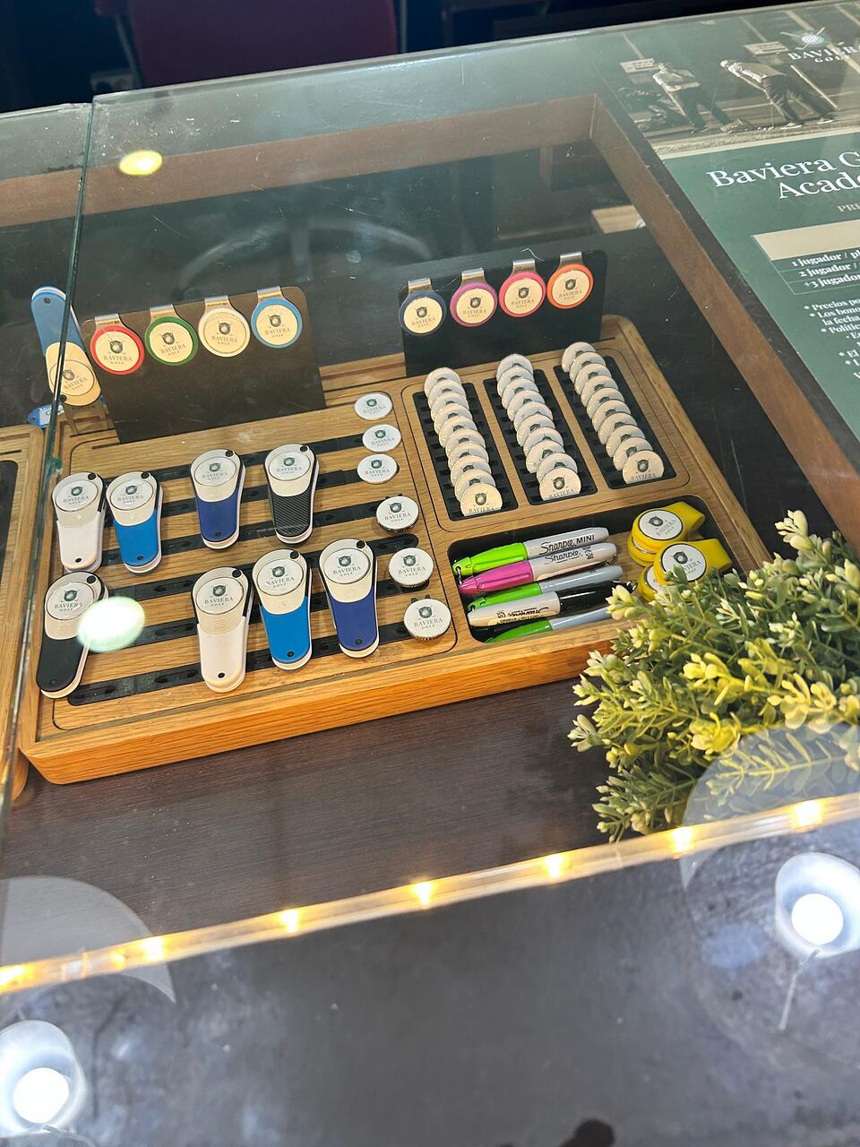 Golf accessories and branded merchandise displayed in a glass counter at Baviera Golf's pro shop.