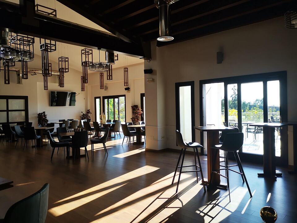 Sunlit dining room at Baviera Golf’s clubhouse, with tables and chairs beside glass doors opening onto a terrace.