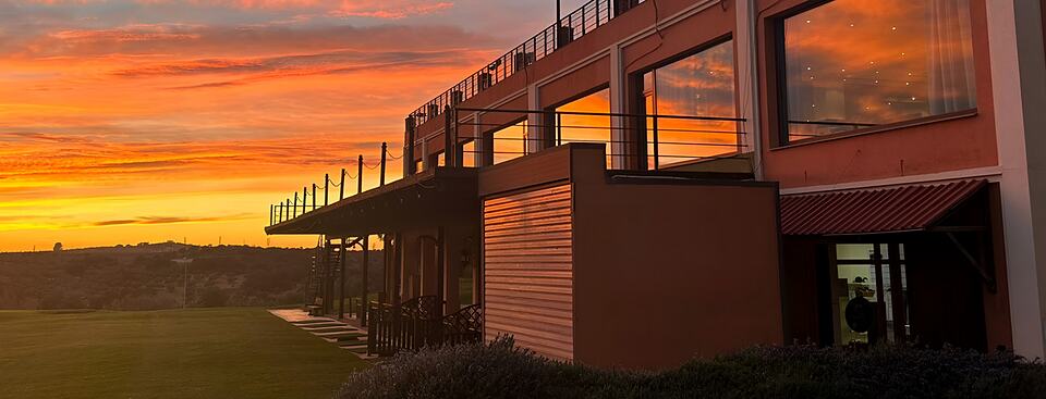 Golf clubhouse terrace silhouetted against a vivid orange sunset