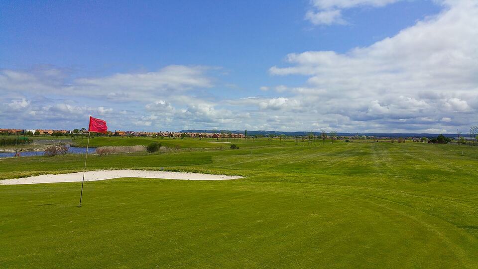 A golf green with a red flag and sand bunker, with the course stretching toward the horizon.