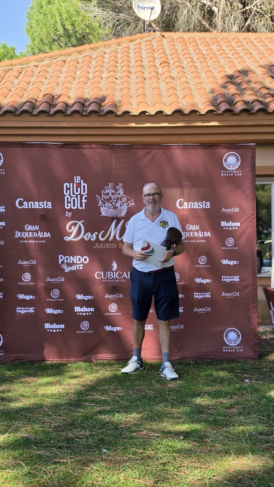 Hombre con un trofeo frente al panel de patrocinadores del torneo Ron 2 Maderas