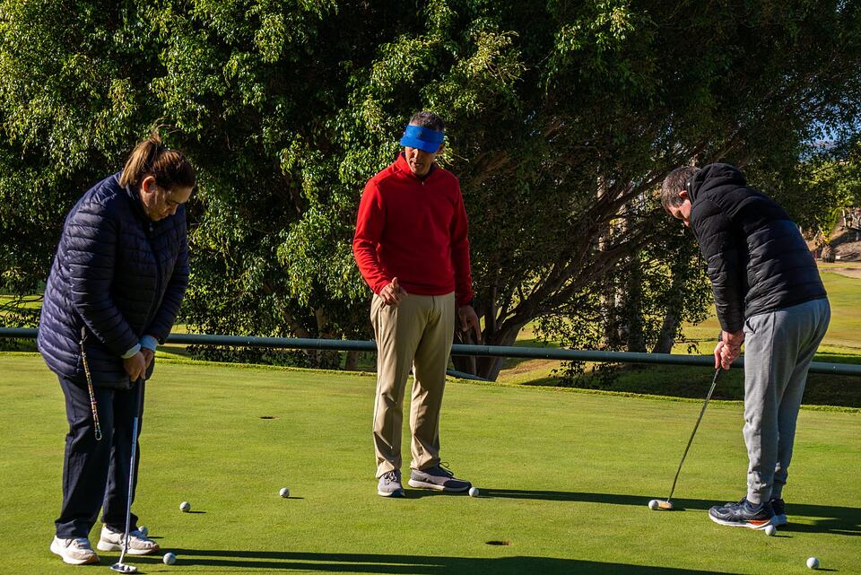 Golf instructor guiding two players as they practise putting on a green at Baviera Golf.