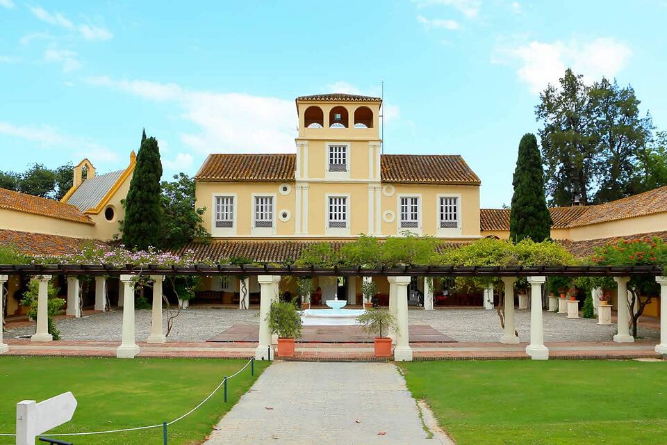 The cream-colored clubhouse with a tiled roof, shaded colonnade and fountain in the courtyard.